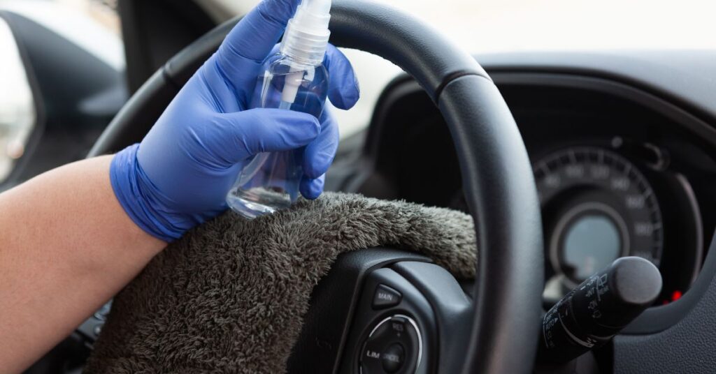 Person using a spray bottle and cloth to clean a steering wheel